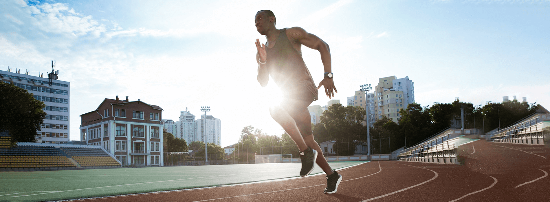 male runner running around a campus track and field with buildings in background